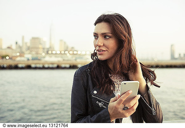 Thoughtful woman holding smart phone with One World Trade Center in background