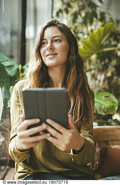 Thoughtful woman holding tablet PC in cafe
