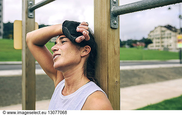 Thoughtful woman leaning against gymnastics bar at park