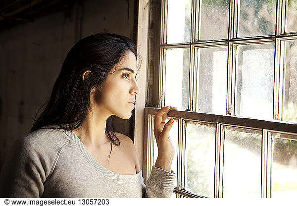 Thoughtful woman looking through window at home