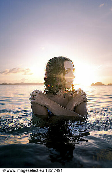 Thoughtful woman self hugging in sea at sunset