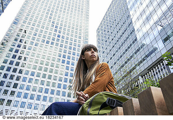 Thoughtful woman sitting in front of modern buildings