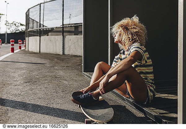 Thoughtful woman sitting with skateboard while looking away on sunny day