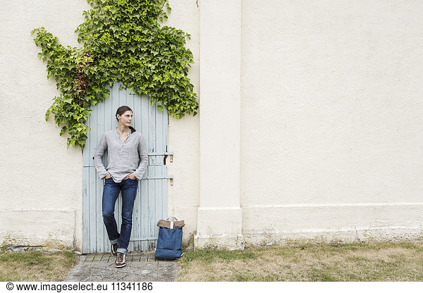 Thoughtful woman standing against closed door with ivy on house wall