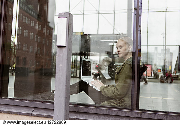 Thoughtful woman using laptop while looking through window at station