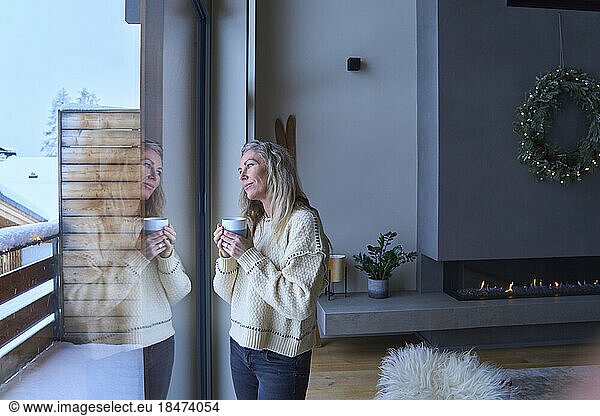 Thoughtful woman with coffee cup looking through window