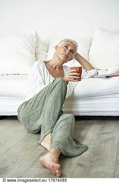 Thoughtful woman with coffee mug leaning on sofa