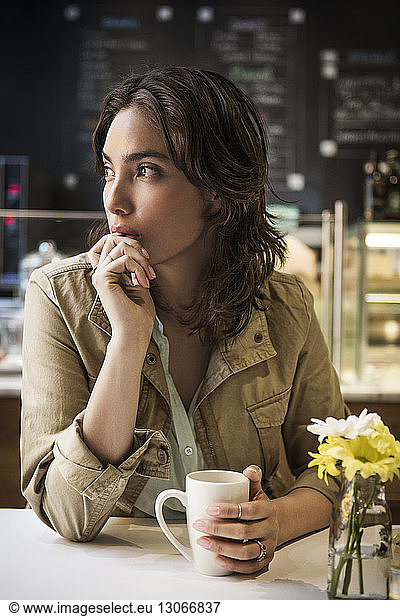 Thoughtful woman with coffee mug sitting at table in cafe