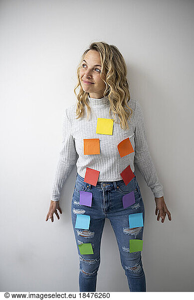 Thoughtful woman with colorful adhesive notes on body near wall