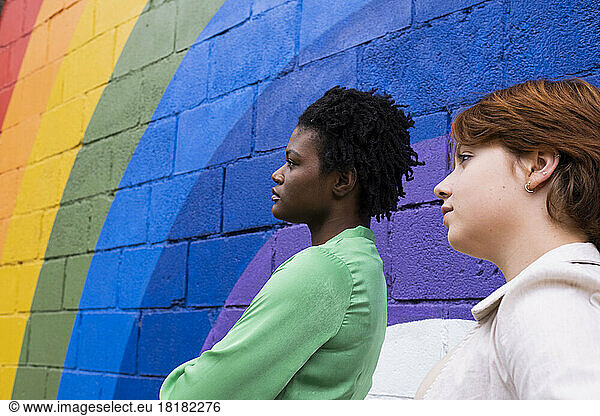 Thoughtful woman with friend by rainbow colored wall