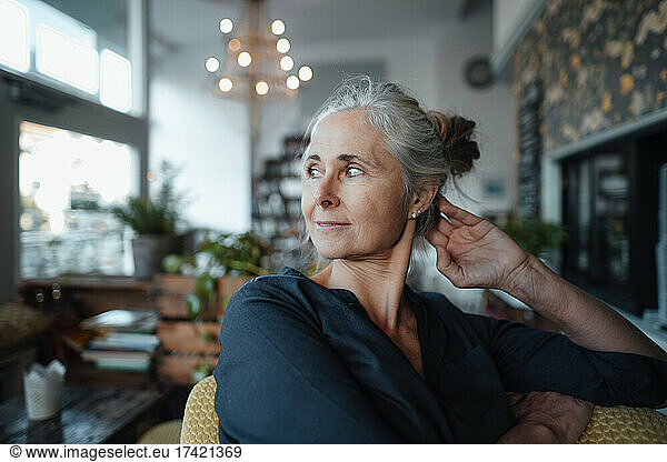 Thoughtful woman with gray hair sitting on chair in cafe