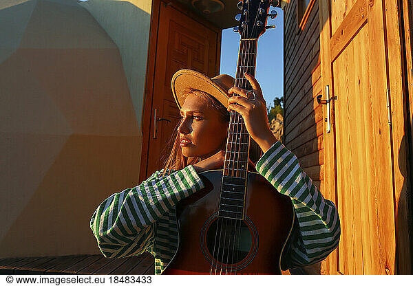 Thoughtful woman with guitar at sunset