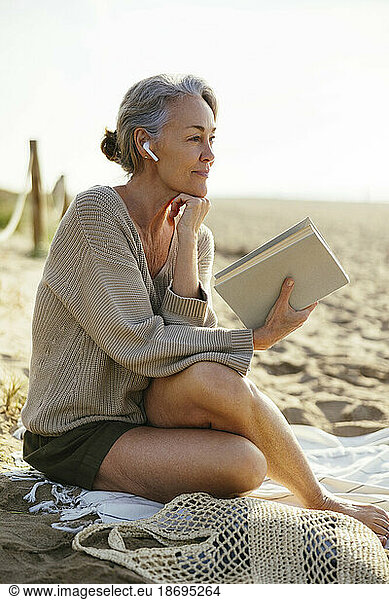 Thoughtful woman with hand on chin holding book at beach