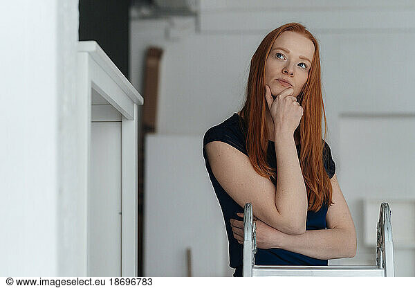 Thoughtful woman with hand on chin standing at office