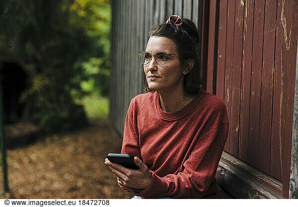 Thoughtful woman with mobile phone sitting in doorway
