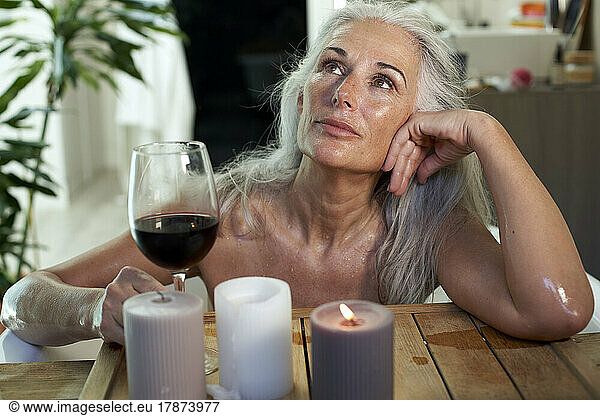 Thoughtful woman with red wine in bathroom