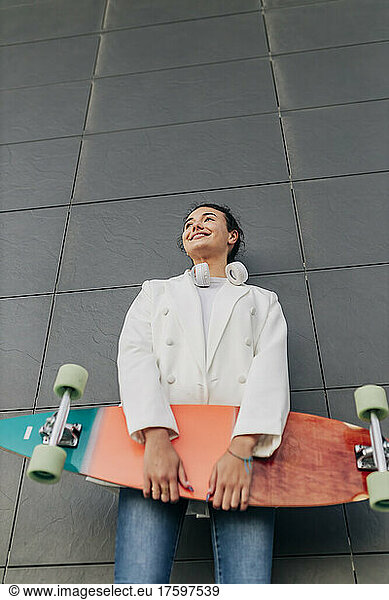Thoughtful woman with skateboard in front of wall