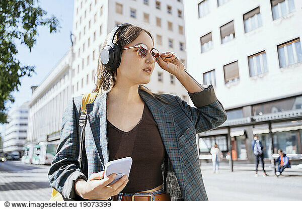 Thoughtful woman with smart phone standing in city