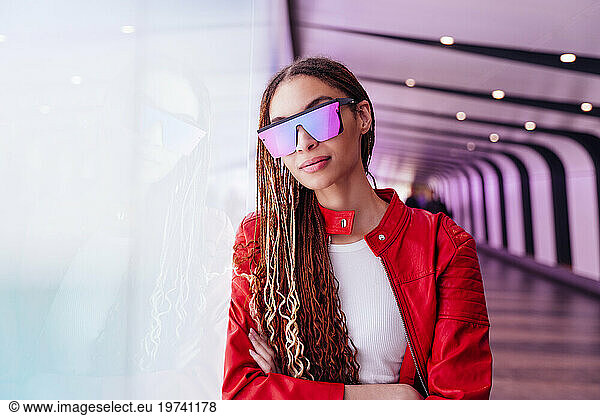 Thoughtful woman with sunglasses leaning on illuminated wall in underground tunnel