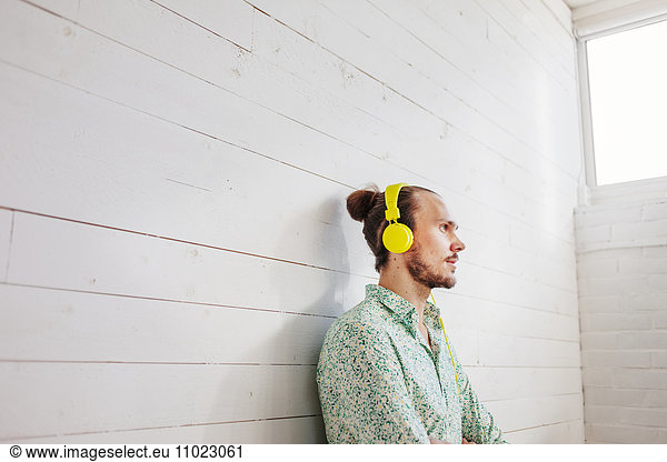 Thoughtful young businessman wearing headphones against wall in office