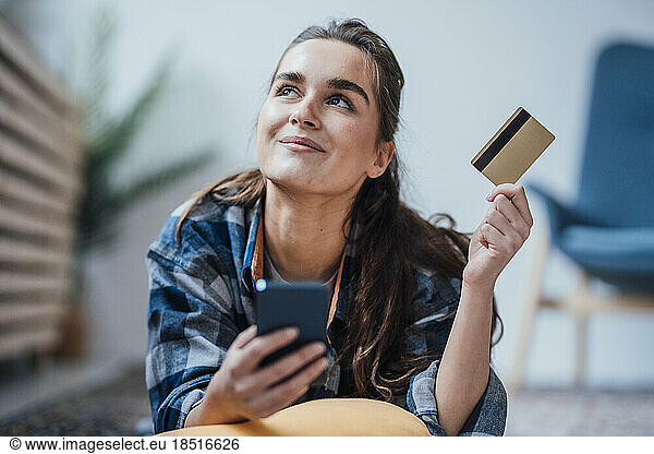 Thoughtful young businesswoman with smart phone and credit card