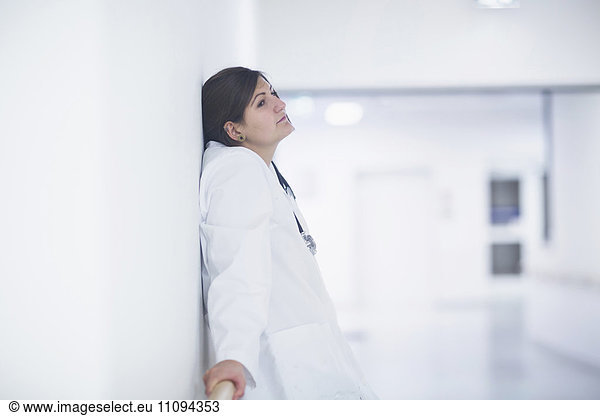 Thoughtful young female doctor leaning against a wall