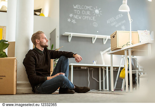 Thoughtful young male entrepreneur sitting on floor at creative office
