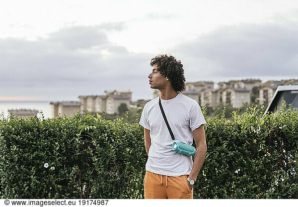 Thoughtful young man with Afro hairstyle standing in front of hedge