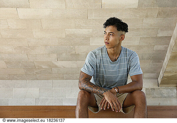 Thoughtful young man with tattooed hand sitting on bench