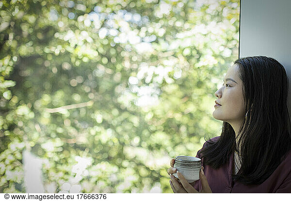 Thoughtful young woman drinking tea and looking out window