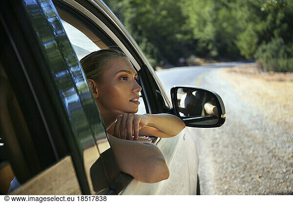 Thoughtful young woman leaning on car window