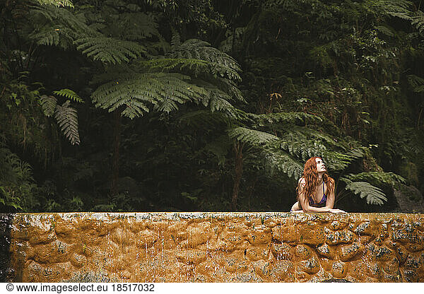 Thoughtful young woman leaning on wall in forest
