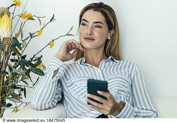 Thoughtful young woman sitting with smart phone on sofa