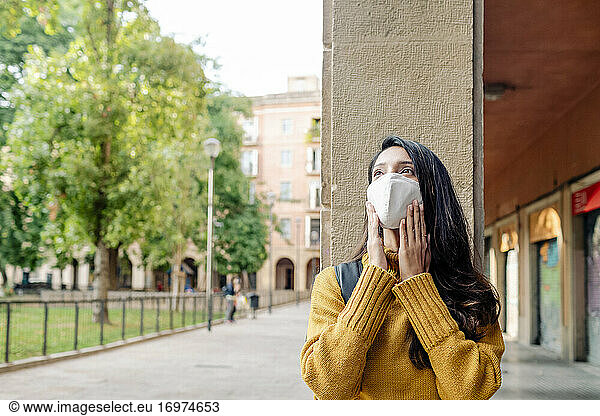 Thoughtful young woman wearing a mask by old buildings in Barcelona