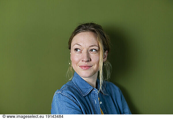 Thoughtful young woman wearing denim shirt in front of green wall