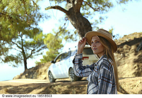 Thoughtful young woman wearing hat standing in front of car
