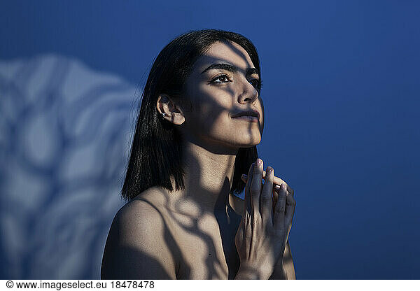 Thoughtful young woman with light on face against blue background