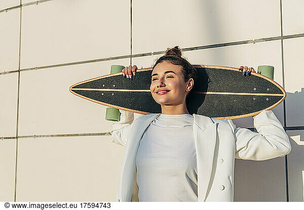 Thoughtful young woman with skateboard in front of wall