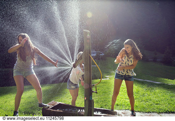 Three adult female friends play fighting sprinkling water hose in garden