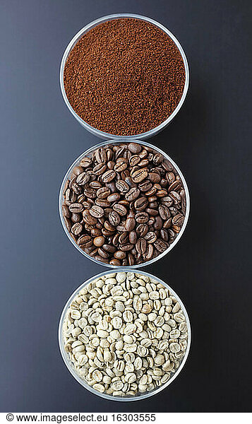 Three bowls with ground coffee  roasted and unroasted coffee beans