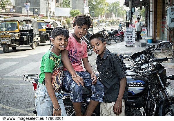 Three boys gather around a motorcycle on a street and are looking at the camera; Amritsar  Punjab  India