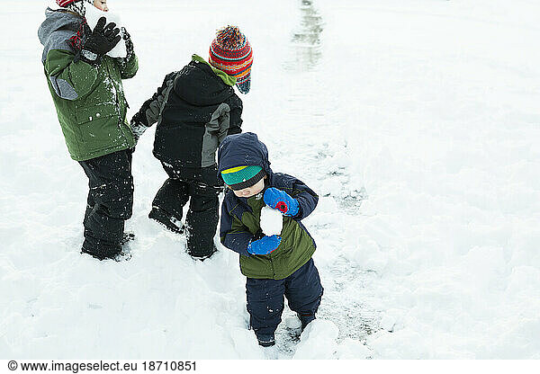 Three brothers play outside making snowballs after winter storm