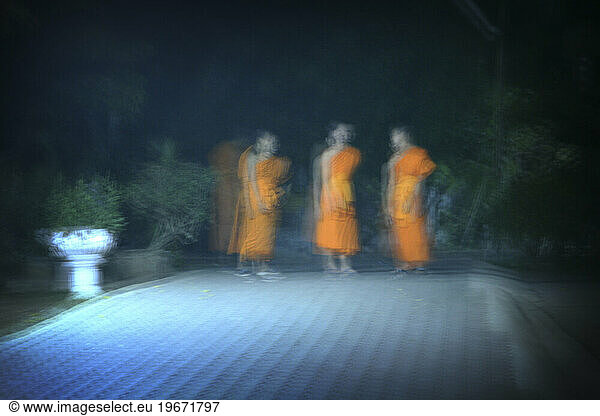 Three Buddhist monks stand in a courtyard at night  lit only by a street lamp. Chiang Rai  Thailand. (Blurred Motion)