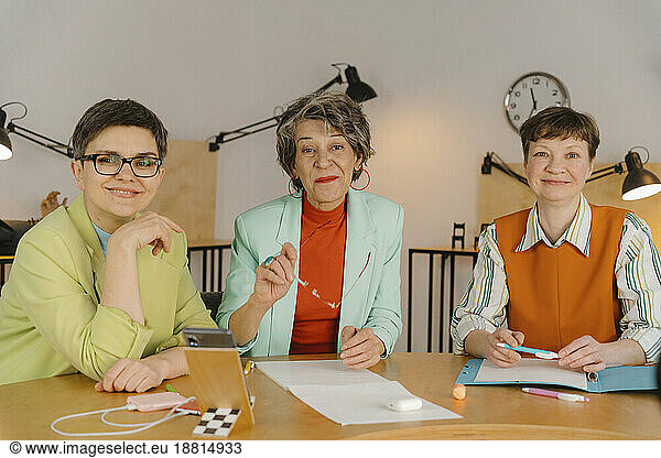 Three business women siting at table looking at camera