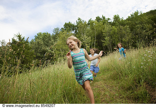 Three children,  girls playing and laughing in the fresh air,  chasing and racing through long grass.