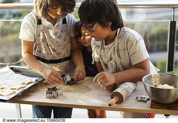Three children cutting out cookies at home