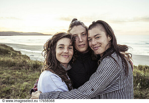 Three close strong female friends hug by the ocean