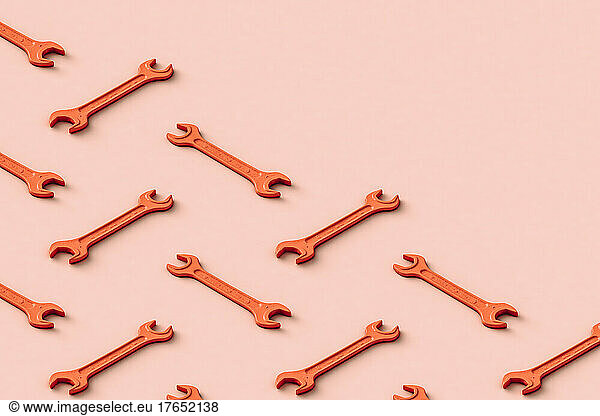 Three dimensional pattern of rows of orange colored wrenches flat laid against beige background