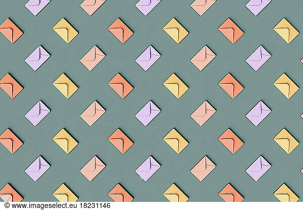 Three dimensional pattern of rows of pastel colored envelopes flat laid against green background
