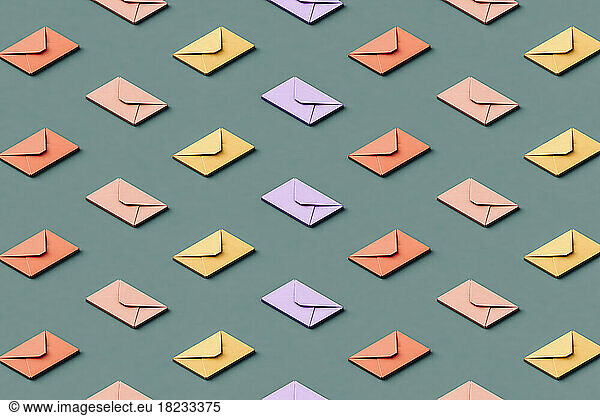 Three dimensional pattern of rows of pastel colored envelopes flat laid against green background